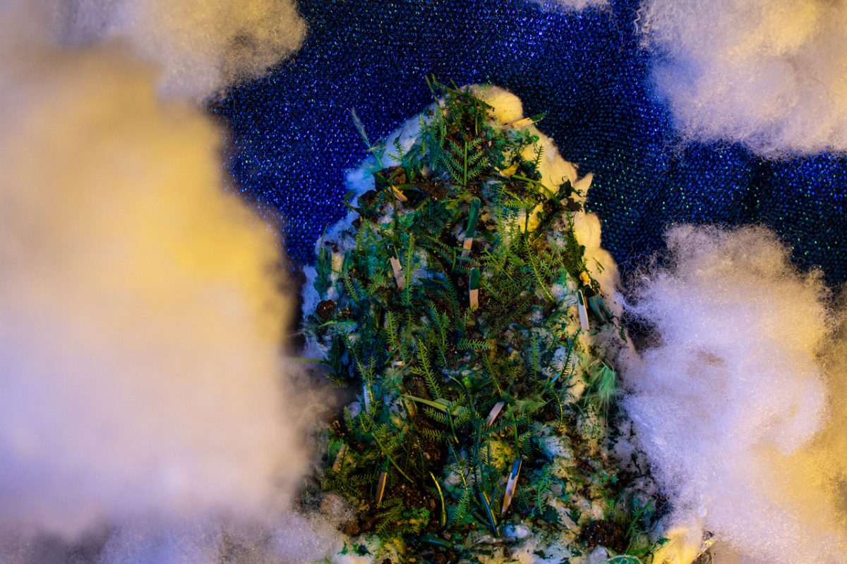 Constructed clouds surround a constructed mountain of greenery and other items