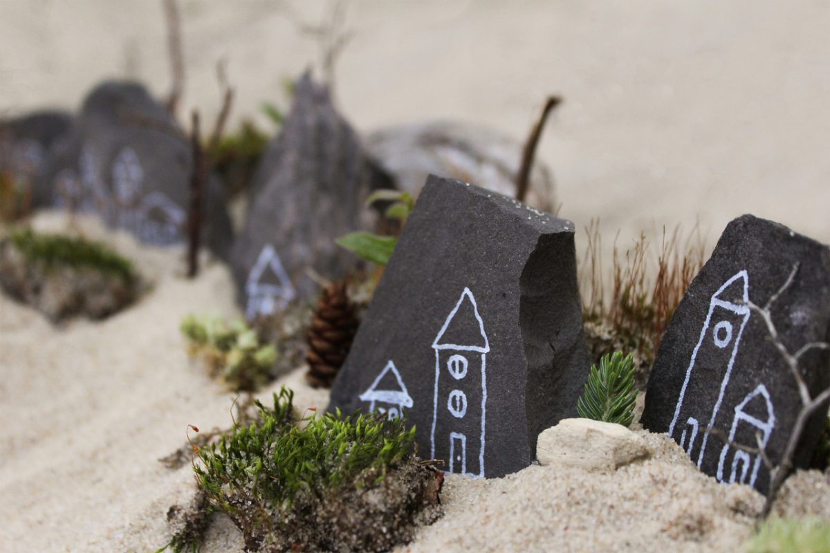 Photograph of white illustrations on dark rocks placed in sand.