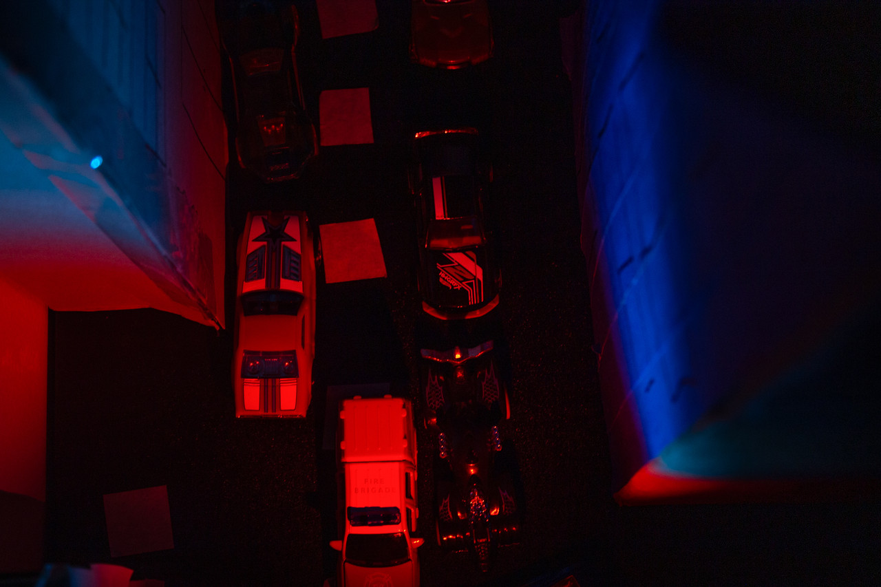 Birds eye view of a street with toy cars and blue/red lighting to cast realistic shadows
