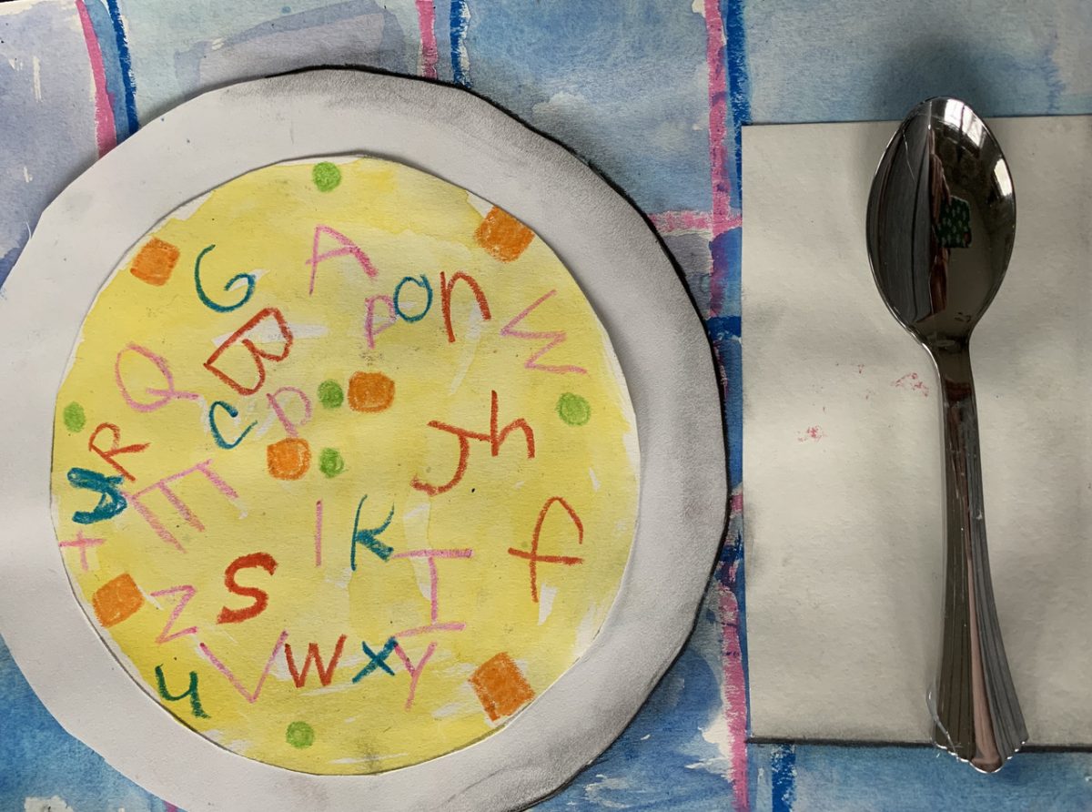 An alphabet soup drawing placed on a plate with a spoon and a colorful place setting