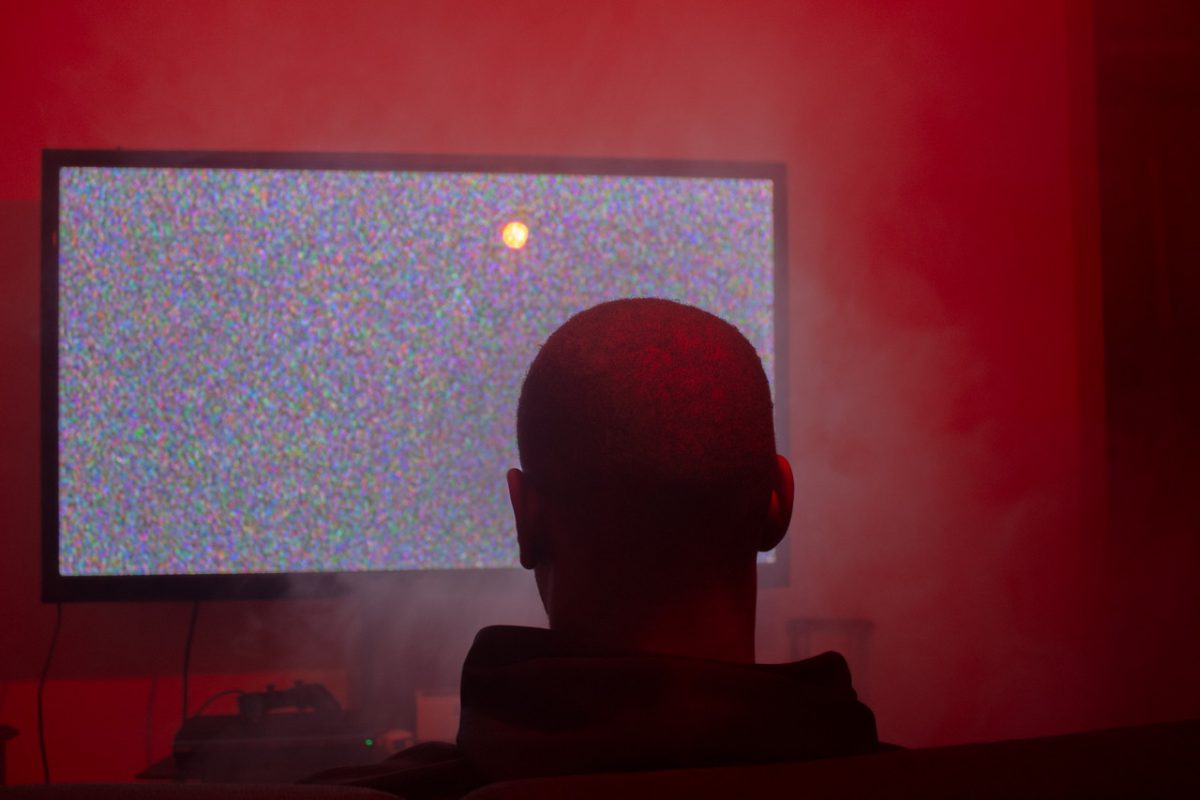 Back of mans head facing a TV playing static visuals while smoke fills the room