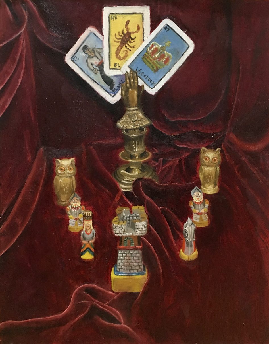 Three Loteria game cards inserted into a holder shaped as a hand, surrounded by figurines and a red drape