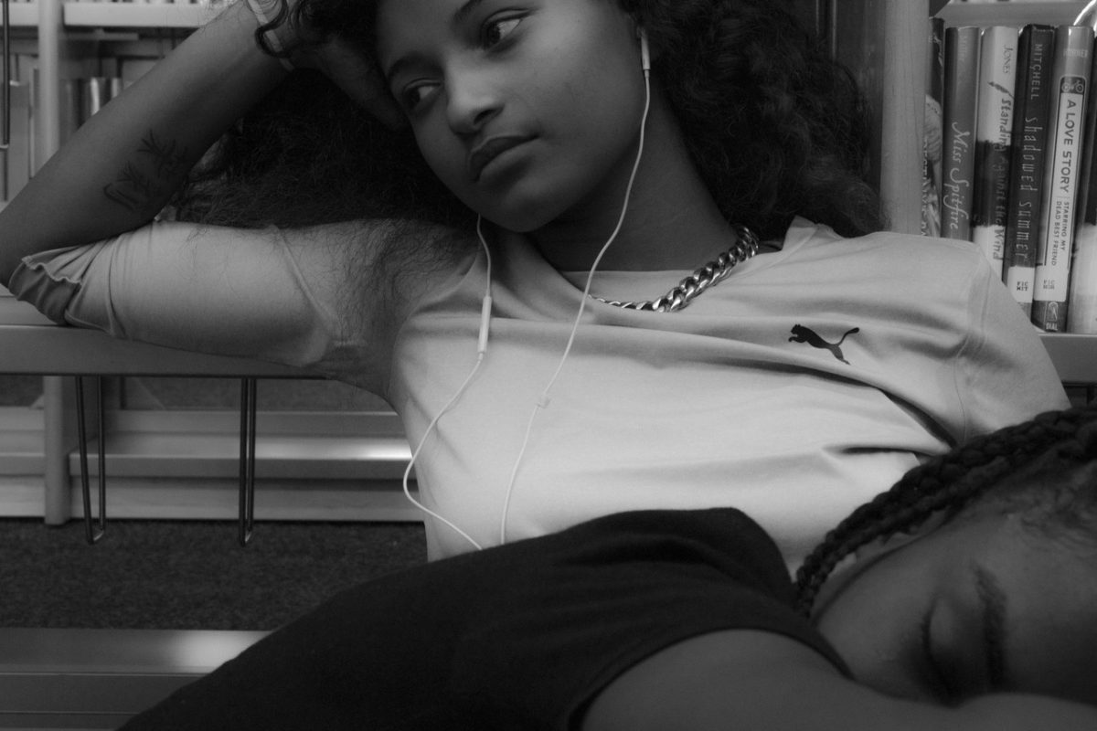 Black and white photograph of person laying across another's lap with books behind them.