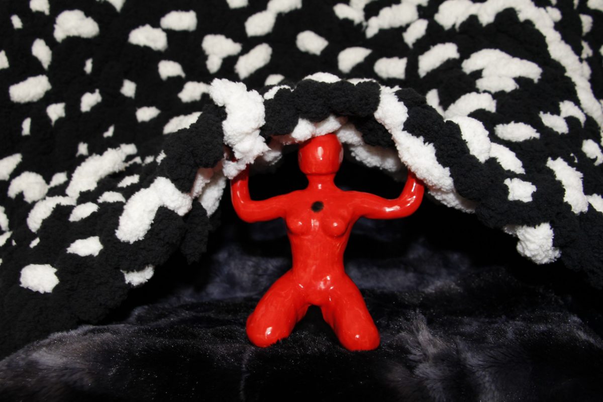 Red figure in center kneels while holding a woven black and white fabric overhead