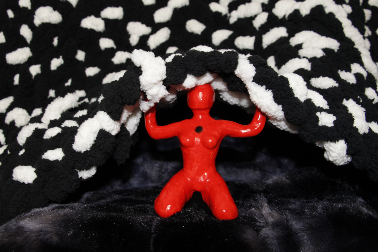 Red figure in center kneels while holding a woven black and white fabric overhead