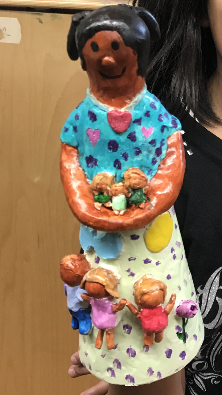 Ceramic of woman with blue shirt and white skirt, 3 children on her skirt and 3 more babies in her arms.