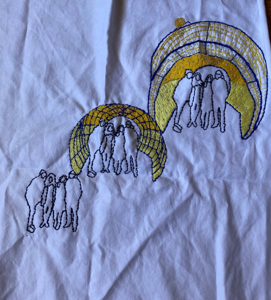 Embroidery on white fabric of 3 groups of people standing together