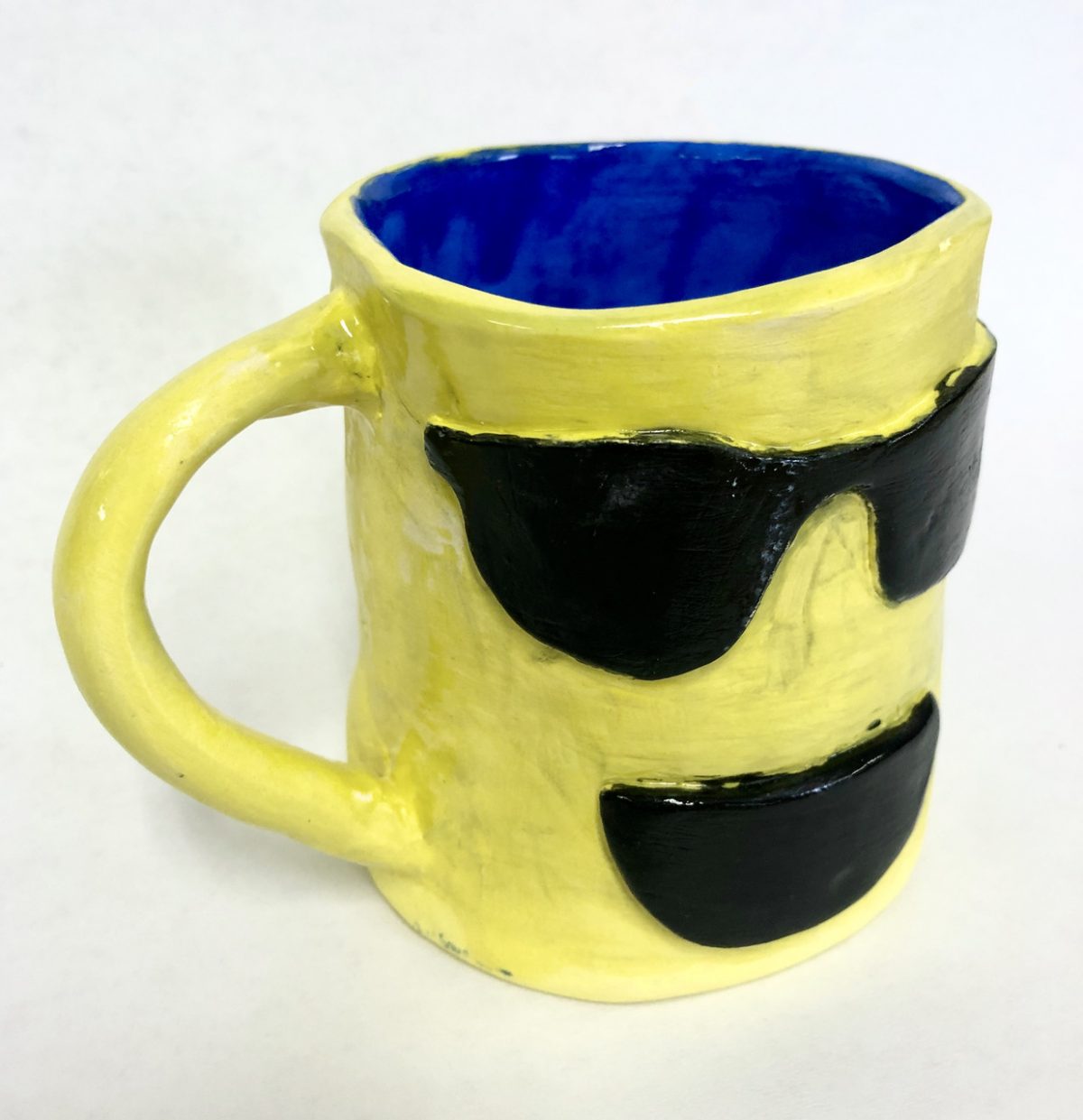 Yellow ceramic mug with smiley face wearing sunglasses. Cobalt blue interior.