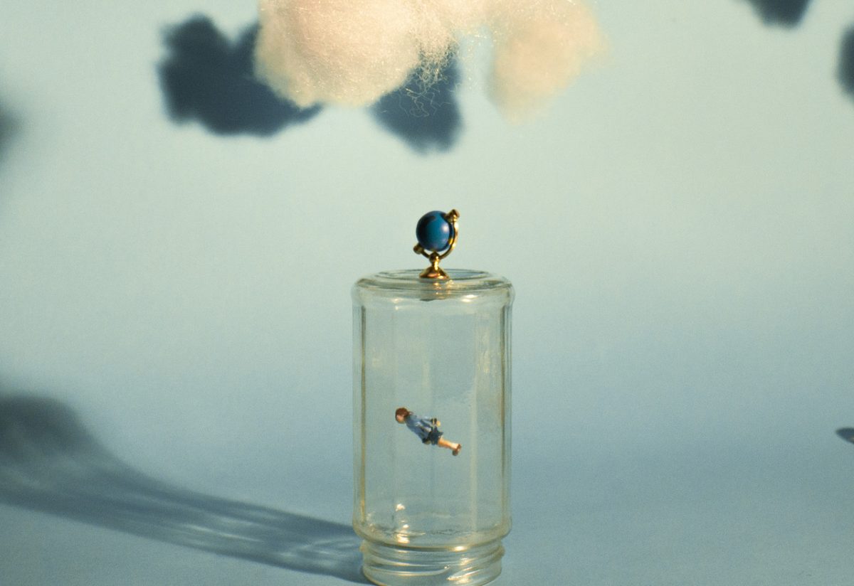 A floating figurine trapped inside a glass mason jar with fake clouds overhead and a baby blue background
