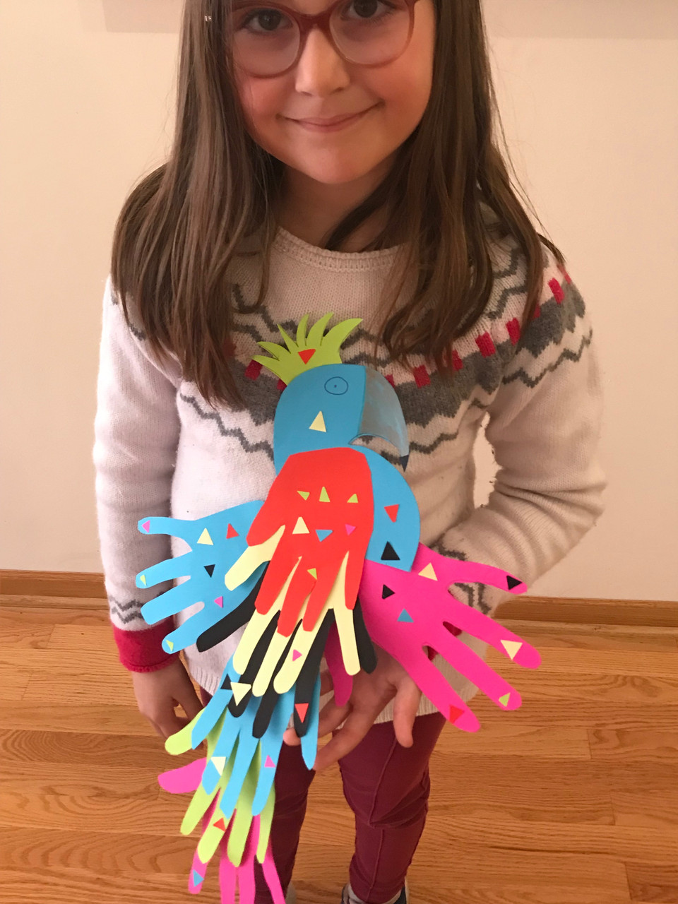 Girl holding colorful parrot sculpture comprised of cut-out paper hands