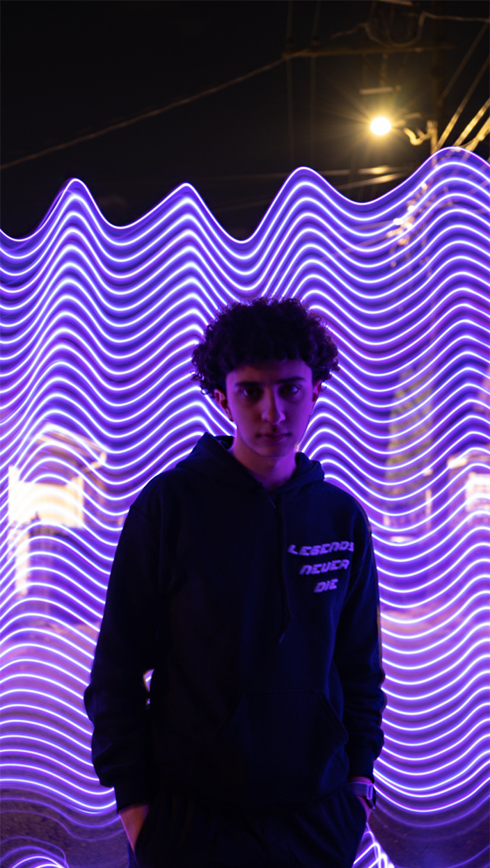 Neon purple lights in a wave behind person looking at camera.