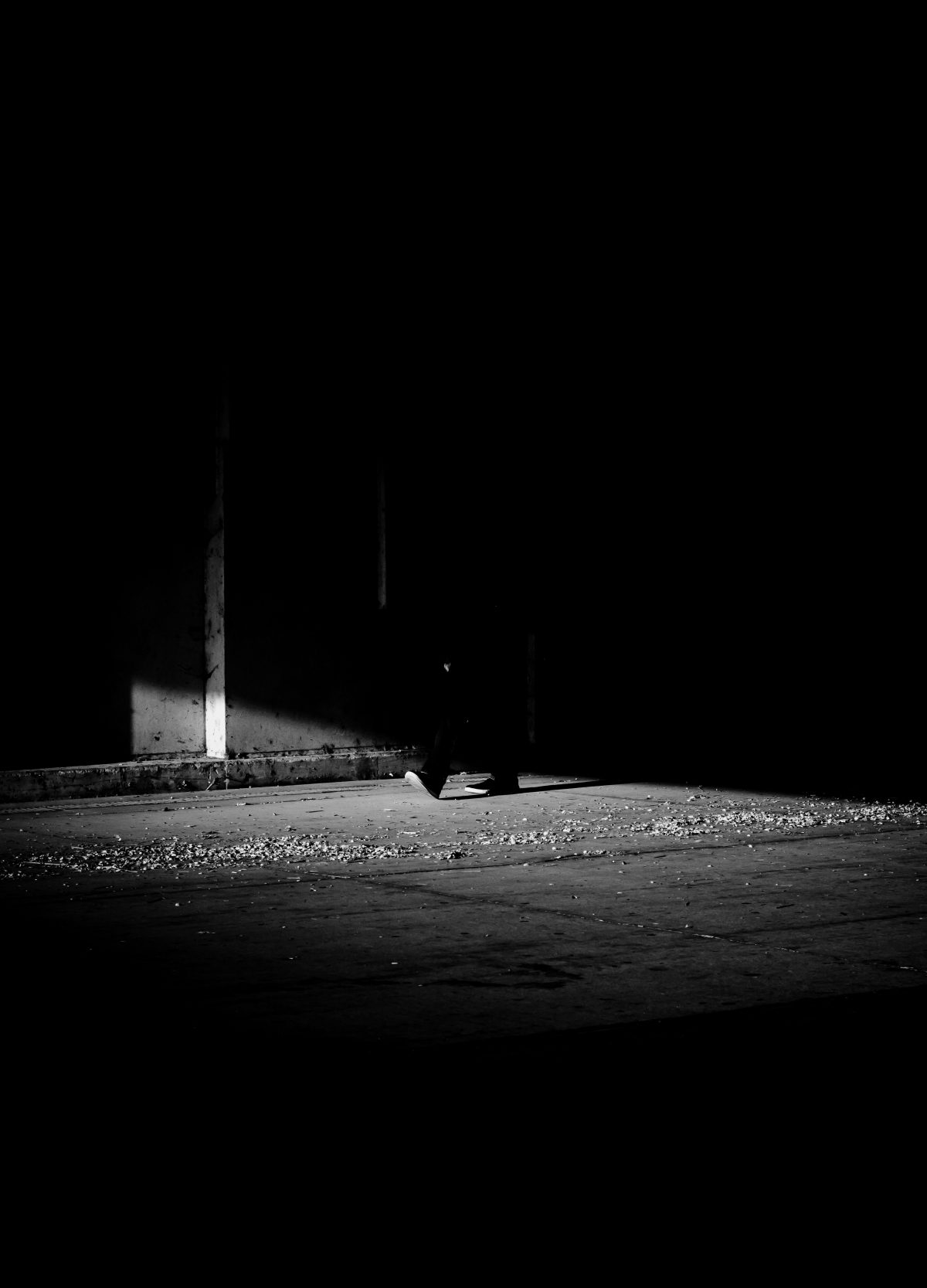 Shadowy view of someone's feet stepping into a sliver of light on a public street.