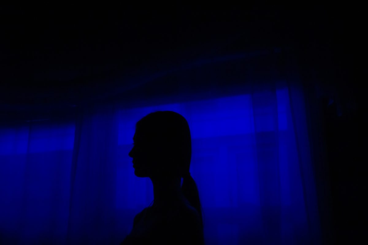 Silhouette of person with ponytail in front of dark blue lit window.