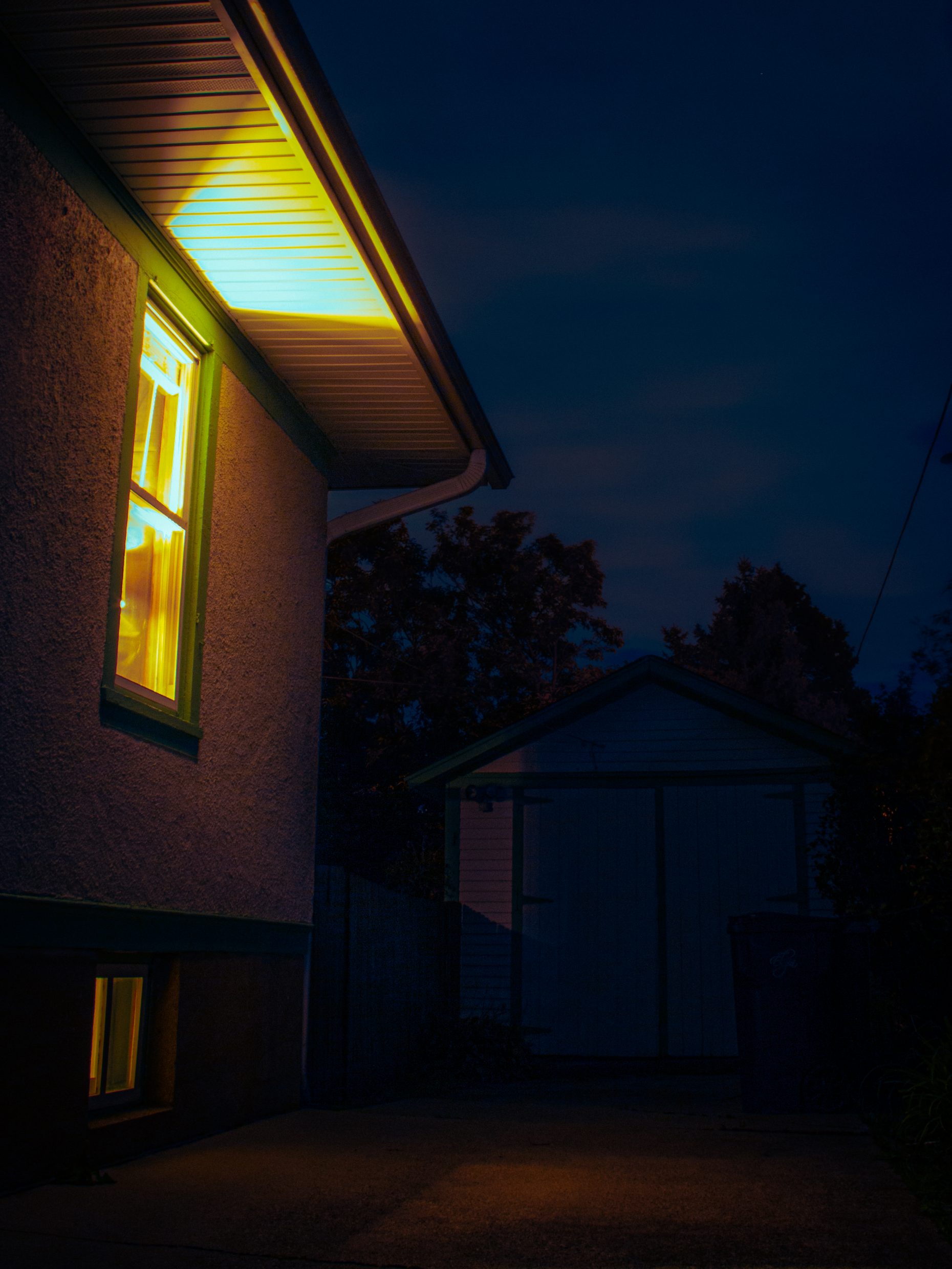 Bright warm light spilling out the window of a house into a dark blue night