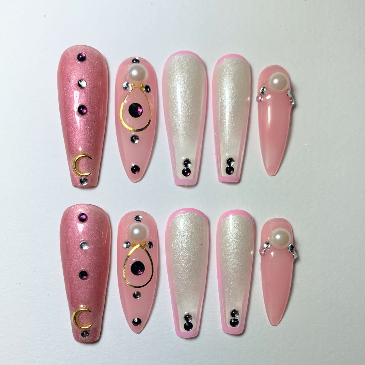 Close-up photo of fake nails painted pink with gem and moon patterns