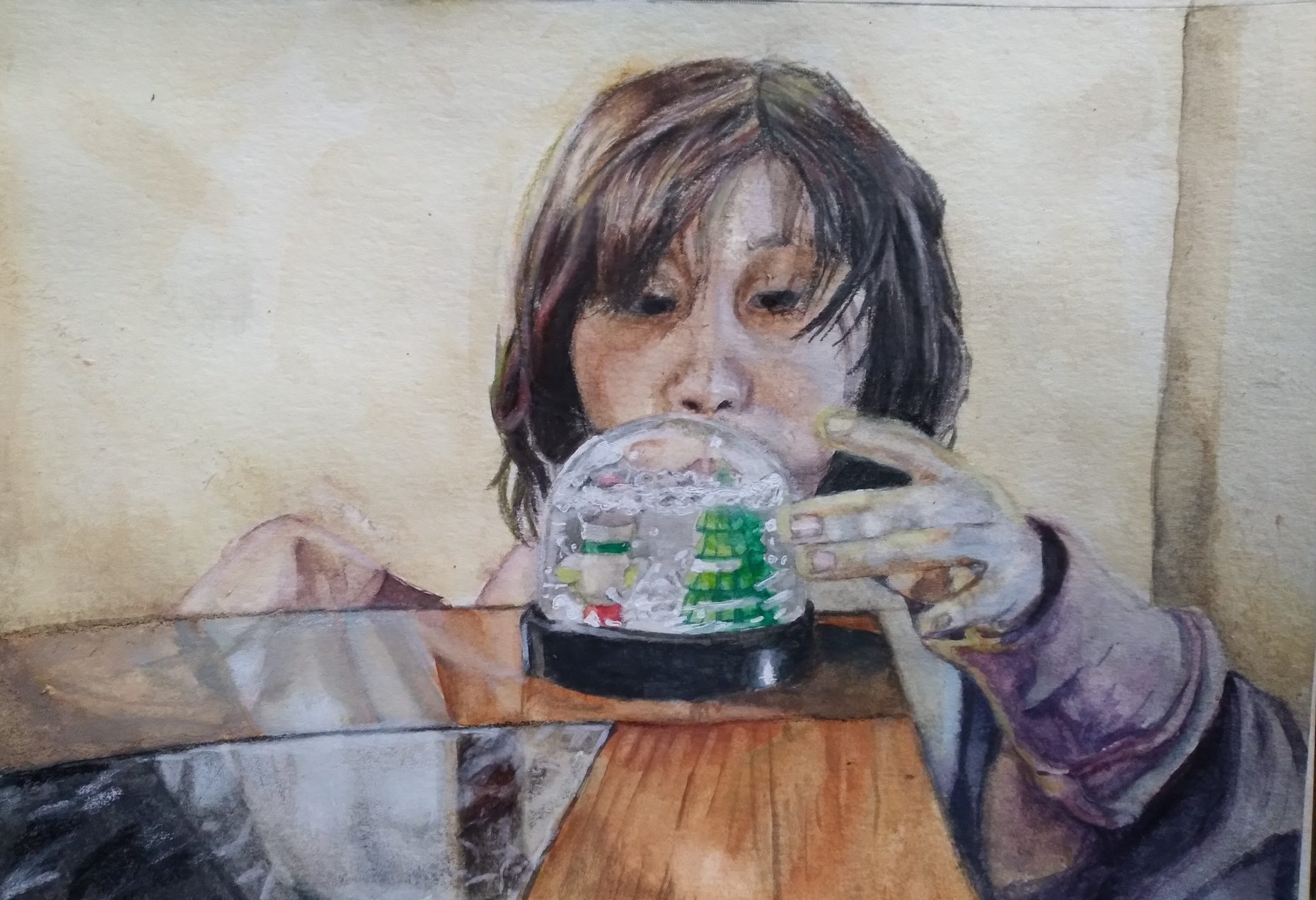 A person looking at a snow glob on a table. A snowman and tree is in the snow globe.