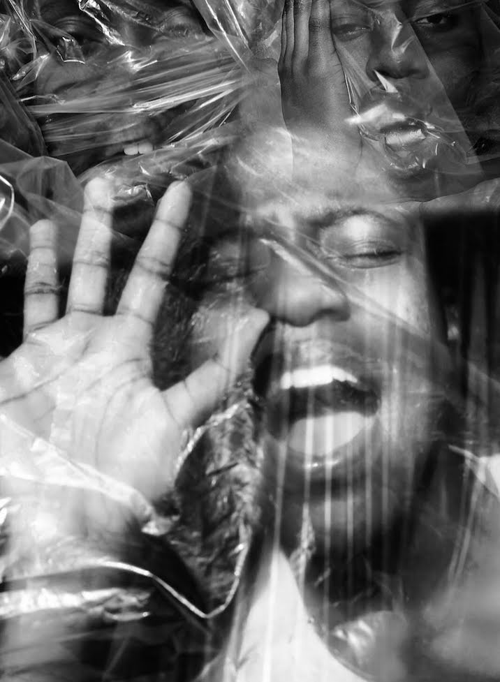 Person with face pressed against plastic, hand out, eyes closed, mouth open. Black and white photograph.