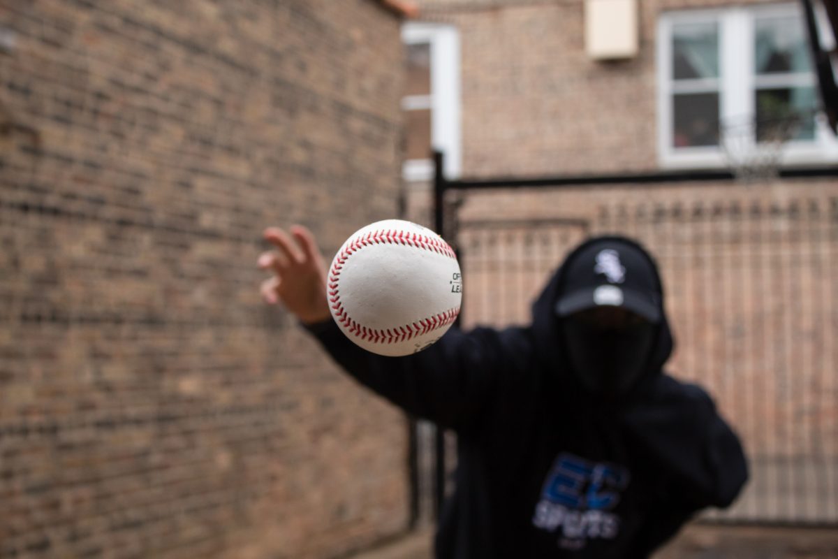 Person wearing black hoodie and hat throwing a baseball at the photographer. Baseball is in focus, rest of image is not.