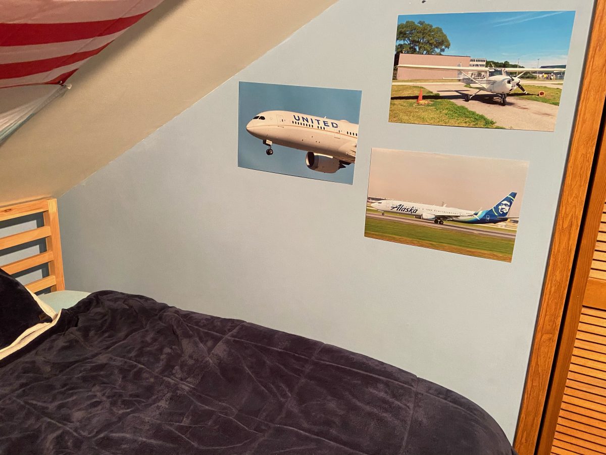 Photograph of a bed with 3 photographs of airplanes hung on the wall next to the bed.