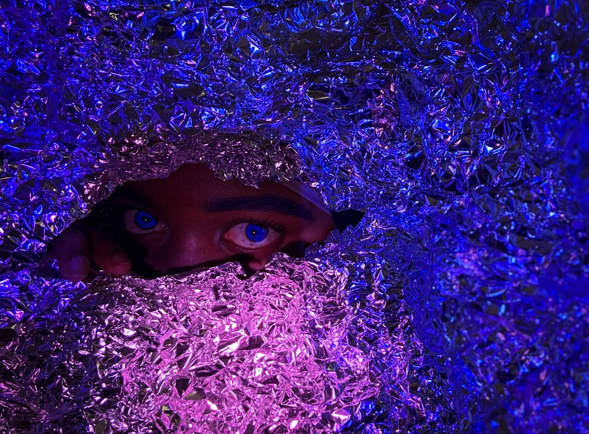 Foil lit with purple and blue light. A hole in the foil has eyes peering out.