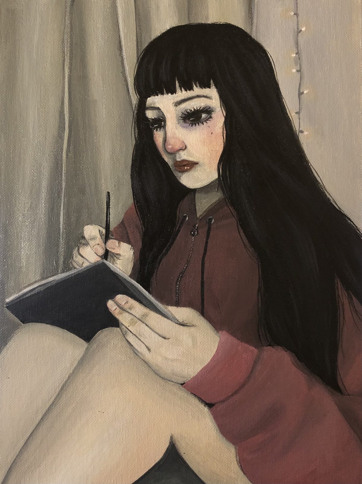 Portrait of someone in a red hoodie sketching while seated in front of some drapery and string lights.