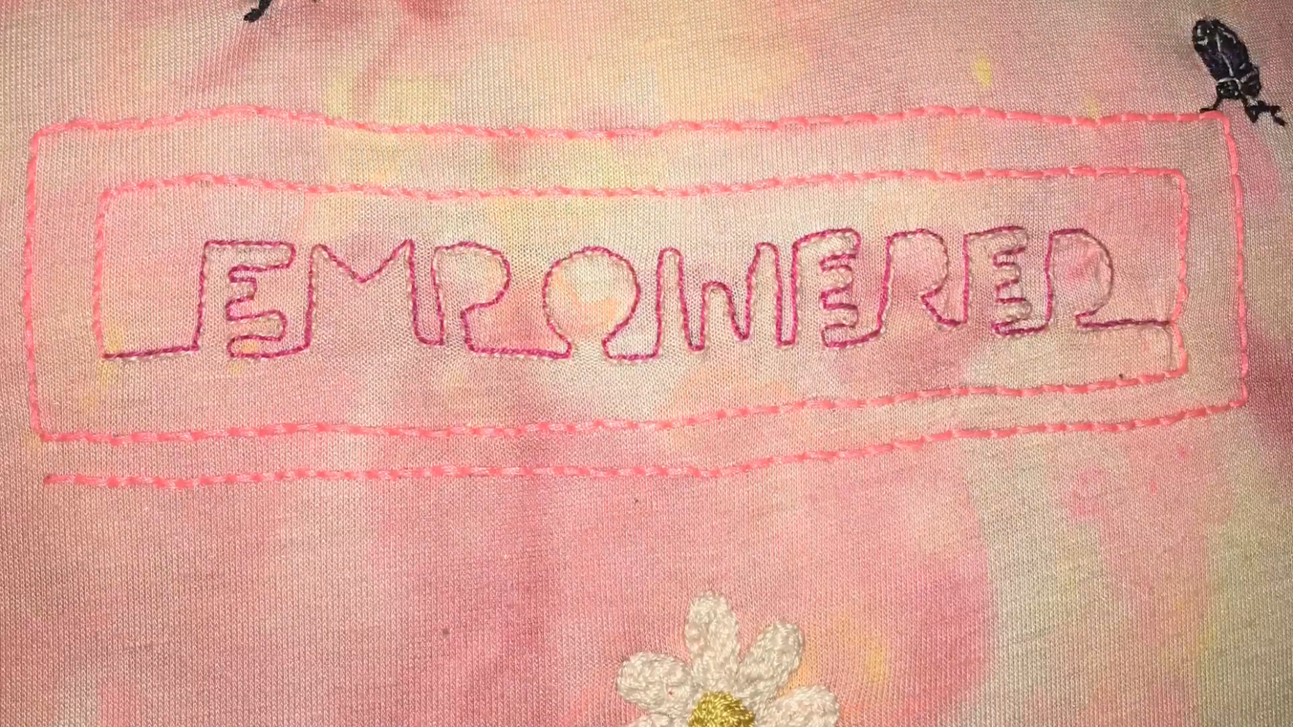 Embroidery of the word "Empowered" on a pink background.