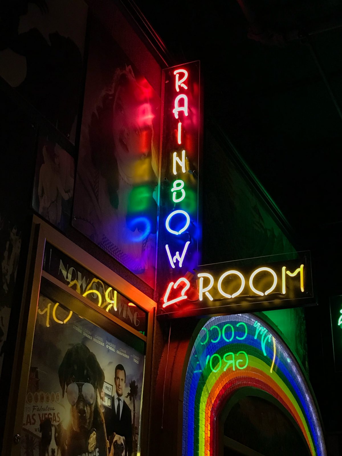 Photo from below of neon sign reading "RAINBOW ROOM" with each letter in different colors; sign is reflected in promotional poster for film screening