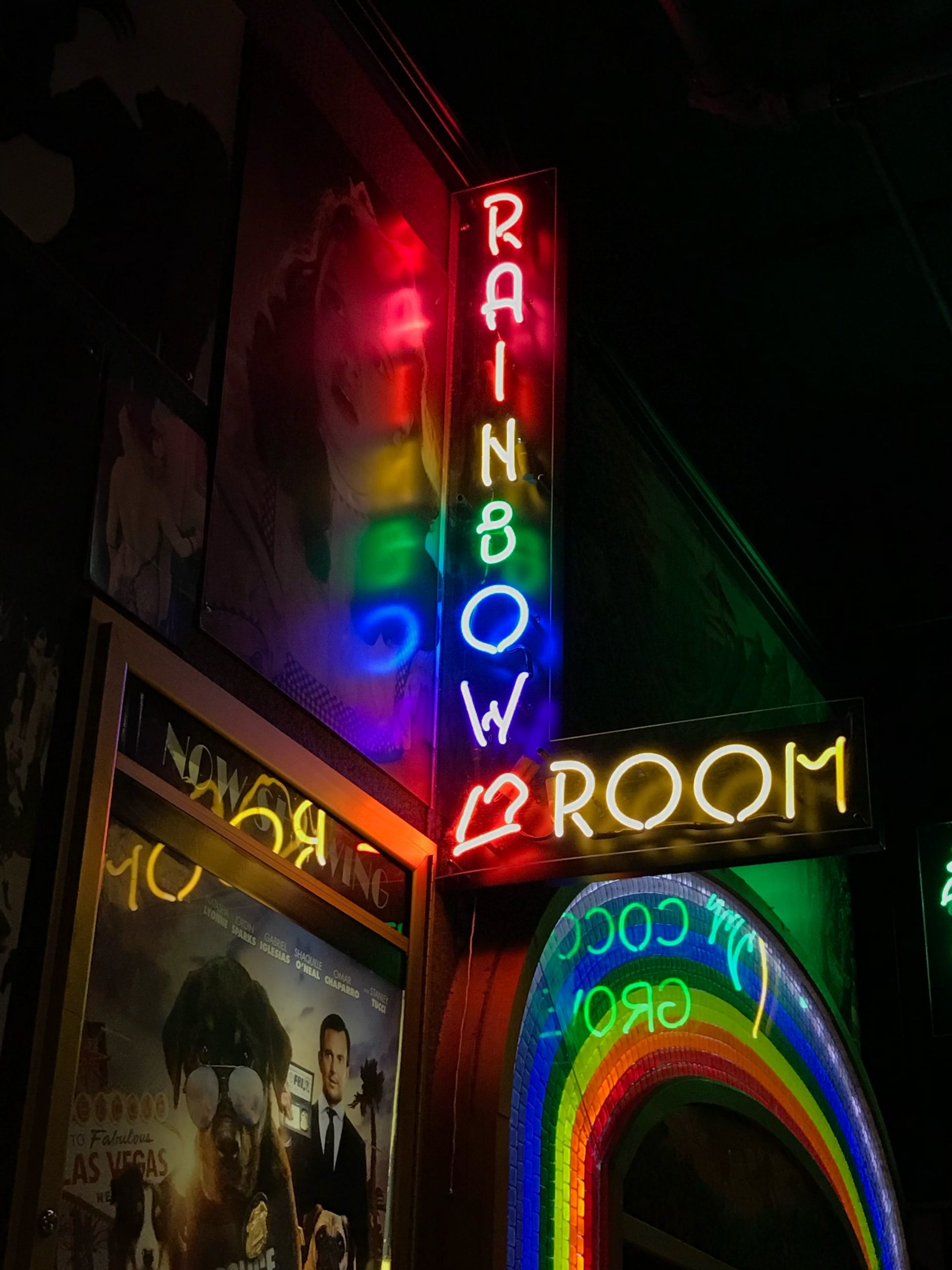 Photo from below of neon sign reading "RAINBOW ROOM" with each letter in different colors; sign is reflected in promotional poster for film screening
