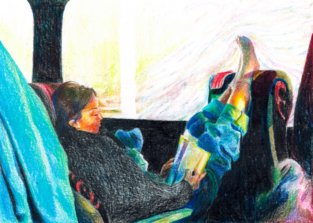 Person in sweater on a charter bus reading a book with her feet up on the seat in front of her.