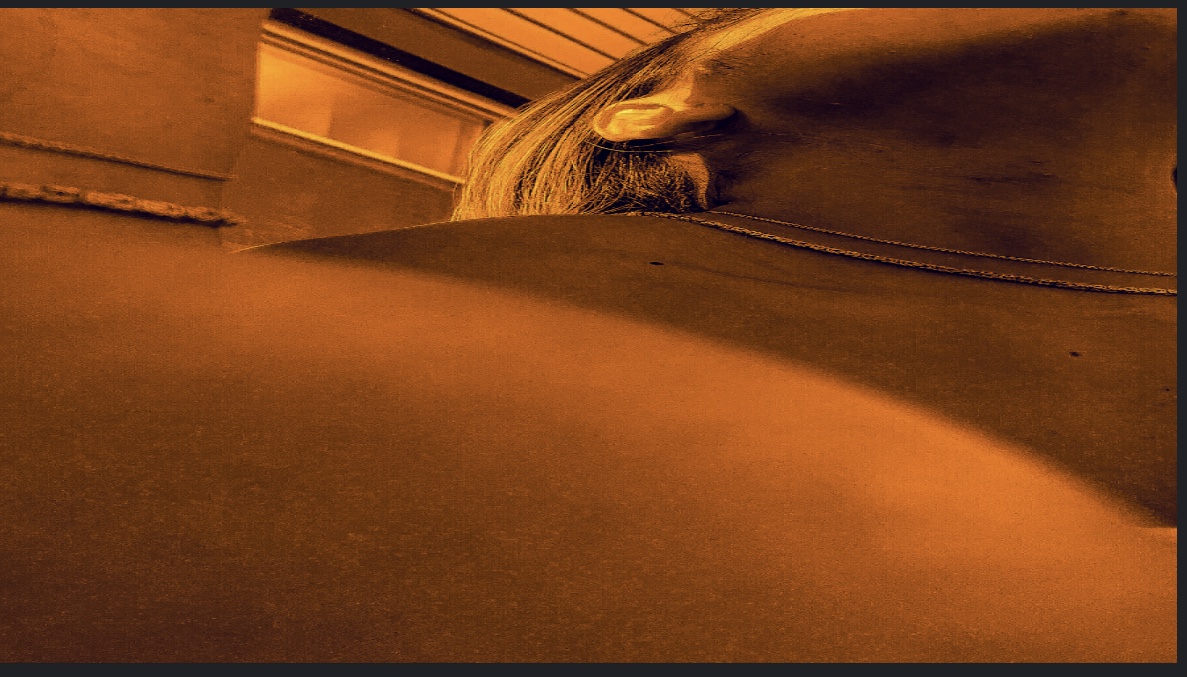 Monochromatic orange photograph at a dramatic angle mainly of the subject's jawline and right ear.