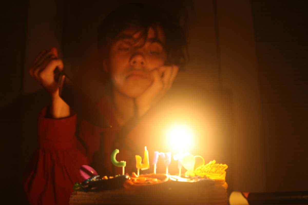 person with knife staring birthday cake with lit candles.