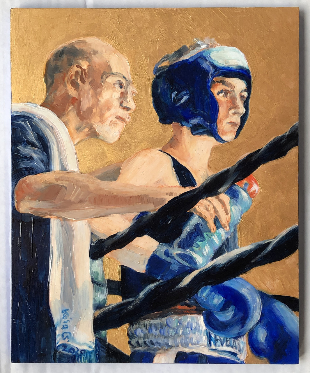Person in boxing ring holding water bottle. Coach stands behind them with a white towel on their shoulder