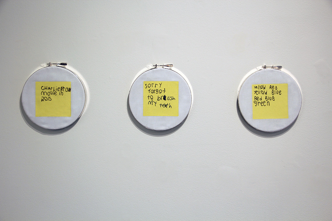 3 hoops with yellow post-it note like squares with text embroidered on them.