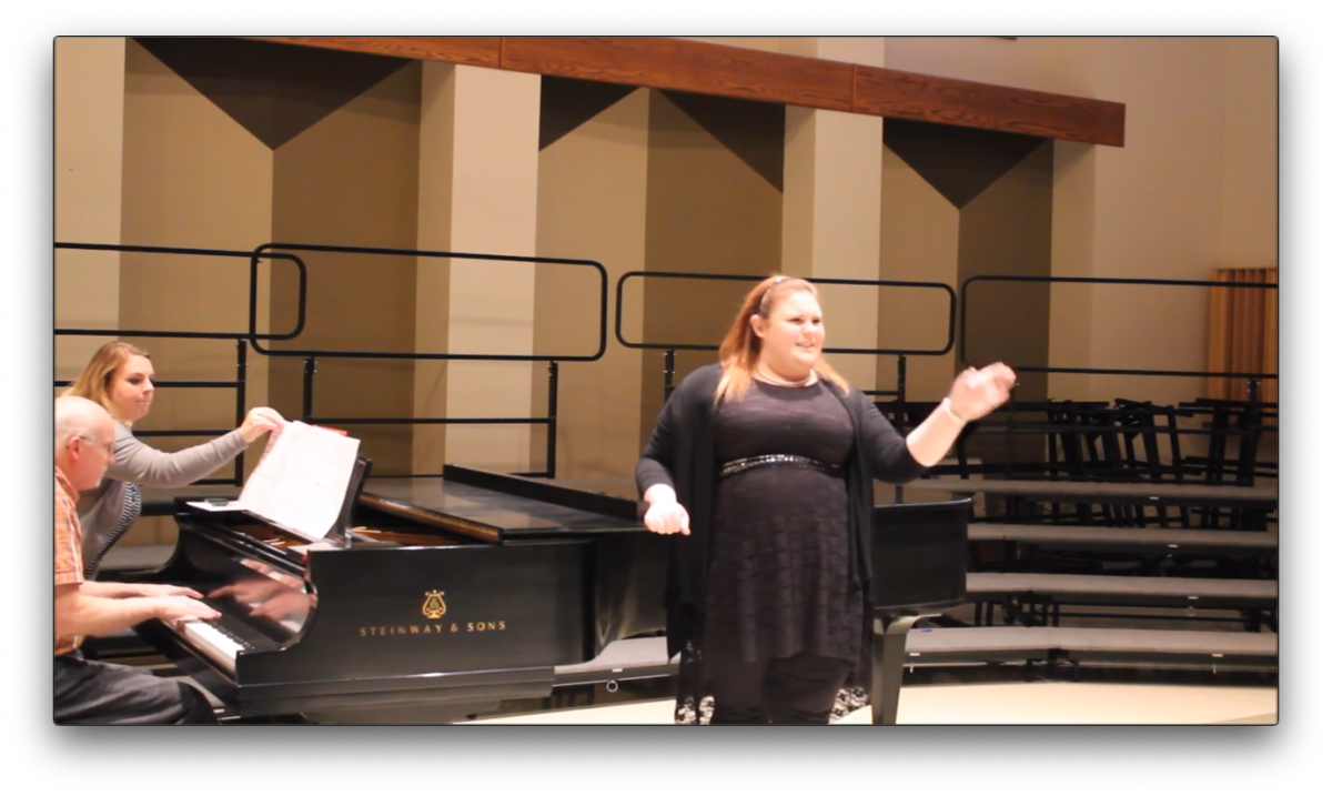 Person playing piano and blonde person with black dress standing in front of piano, singing