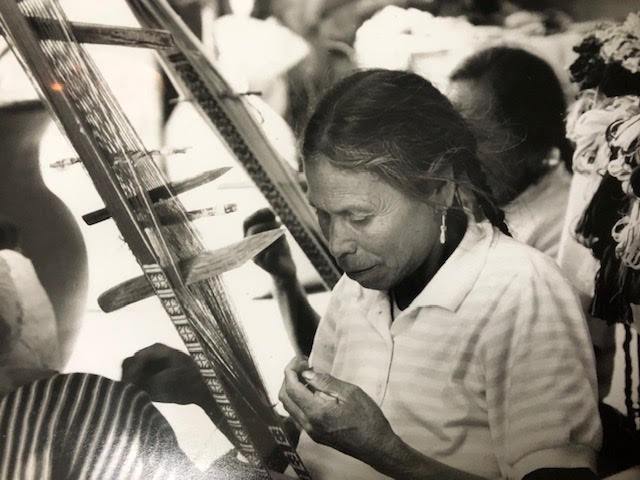 Black and white photograph of a person in a striped shirt at a handloom, weaving.