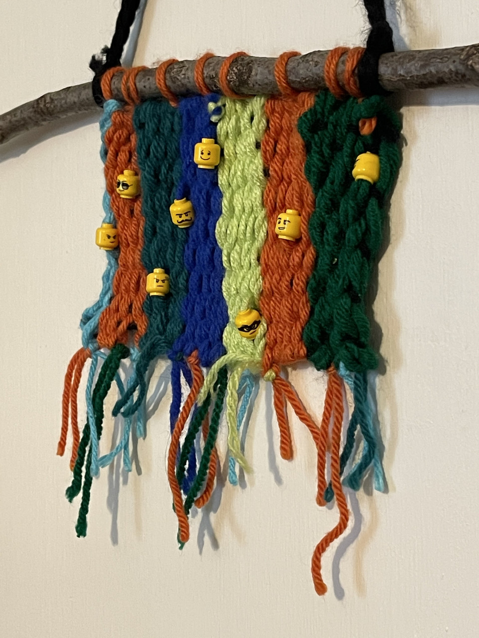 A yarn weaving with little lego heads beaded onto the yarn