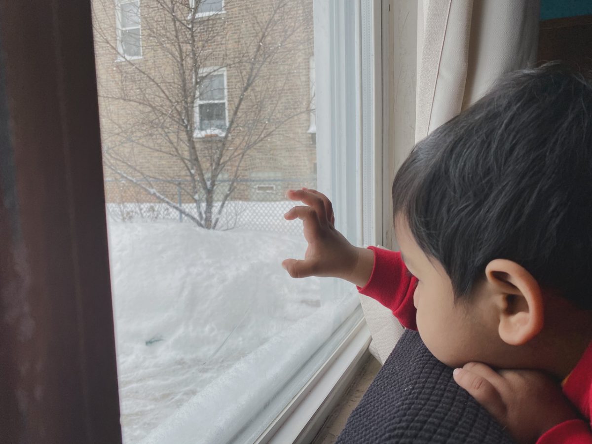 Photograph of a child with his hand on a window and snow outside