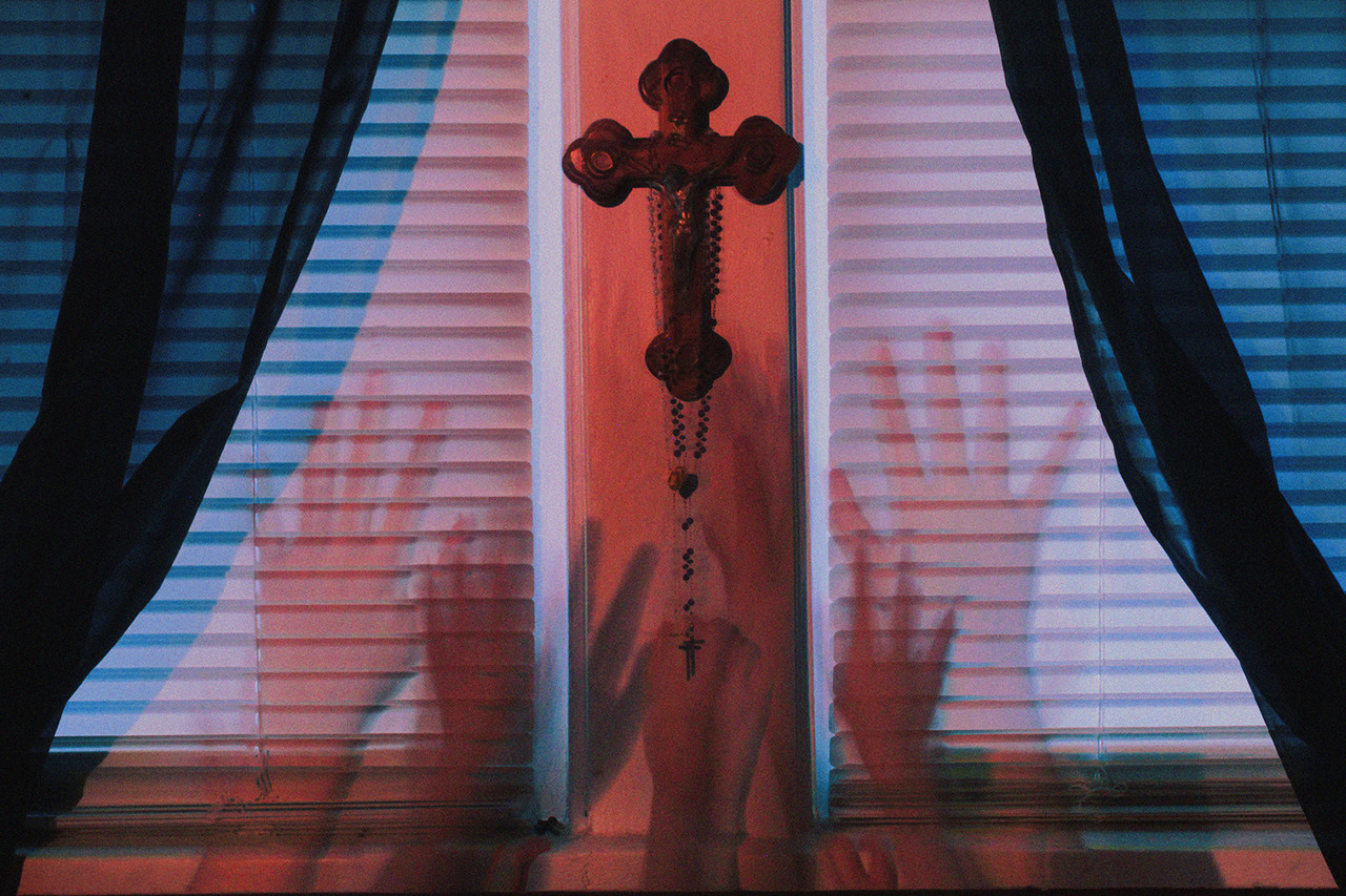 Photograph of the shadows of hands on a window with a cross between them