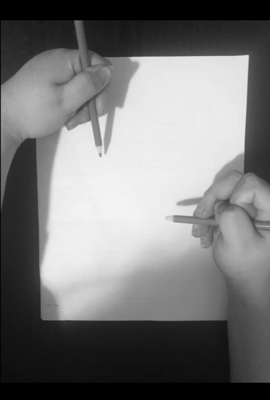 A black and white photo of a piece of paper with two hands holding pencils