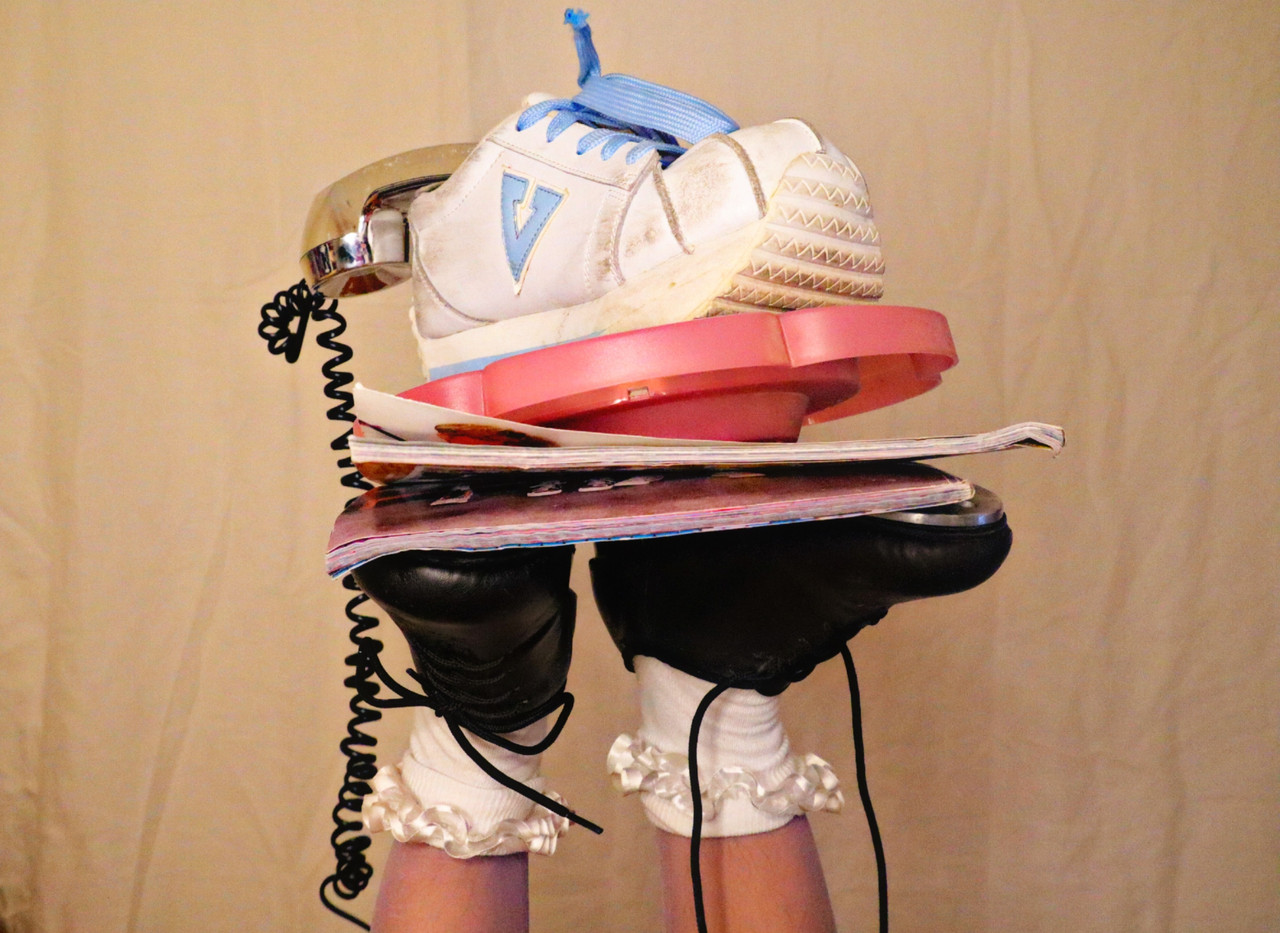 A photograph of a phone, a shoe, and other objects being balanced by someones feet.