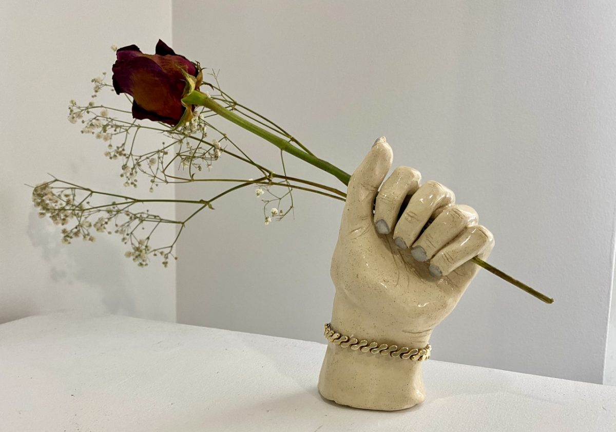 A ceramic hand with a closed fist holding a rose and stem of small flowers