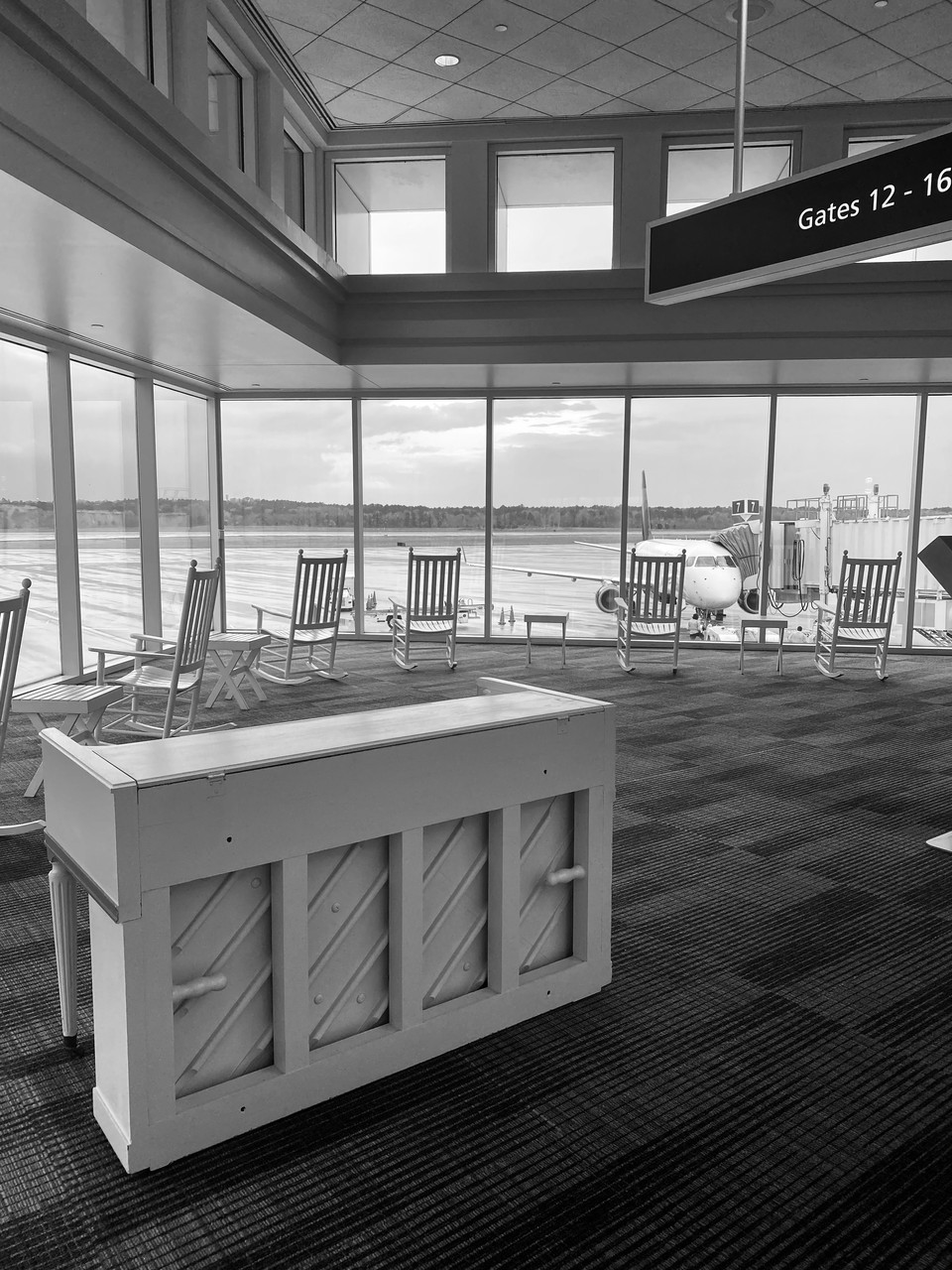 Black and white photograph of airport waiting area with upright piano.