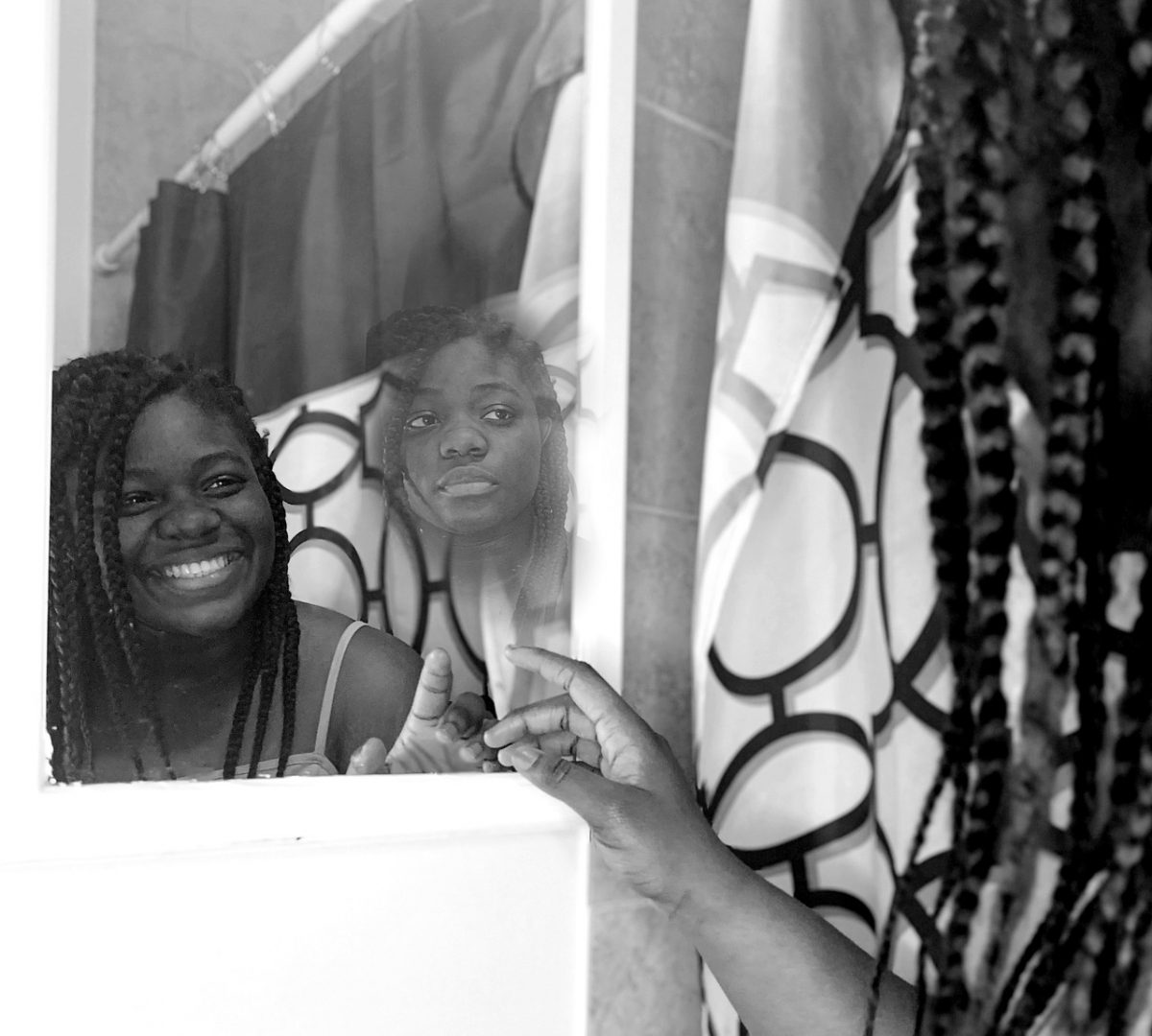 A black and white photo of a girl smiling in the mirror with another faded face looking sad