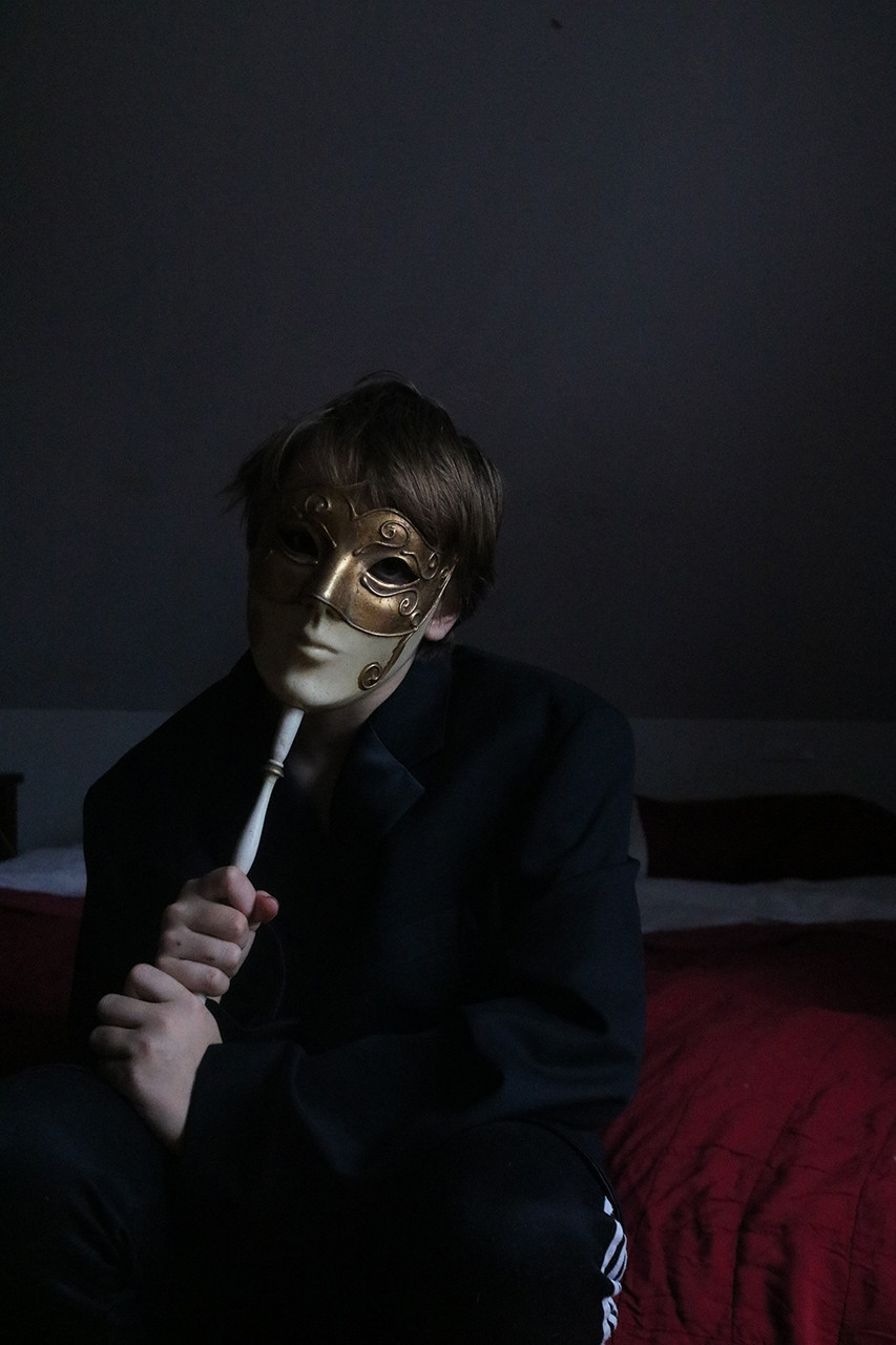 Dark photograph of a teen holding a mask over their face
