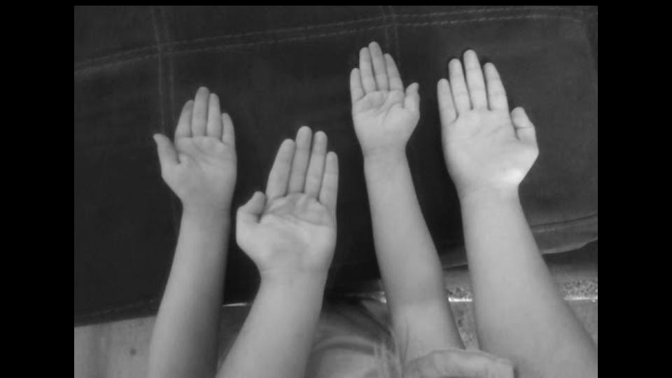 A black and white photo of four hands stretched out
