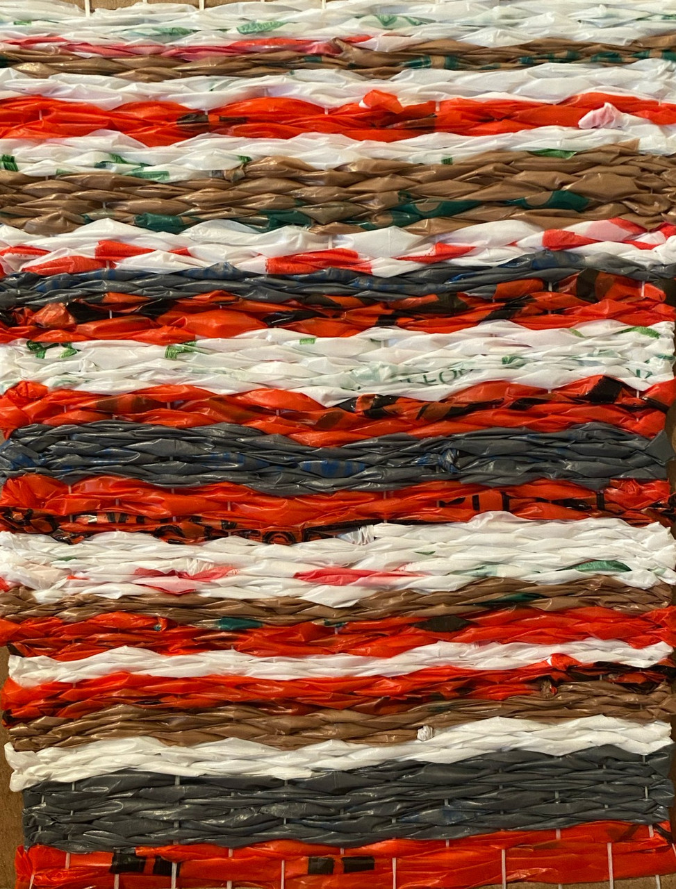 Plastic bag weaving with red, white, browns, and grays