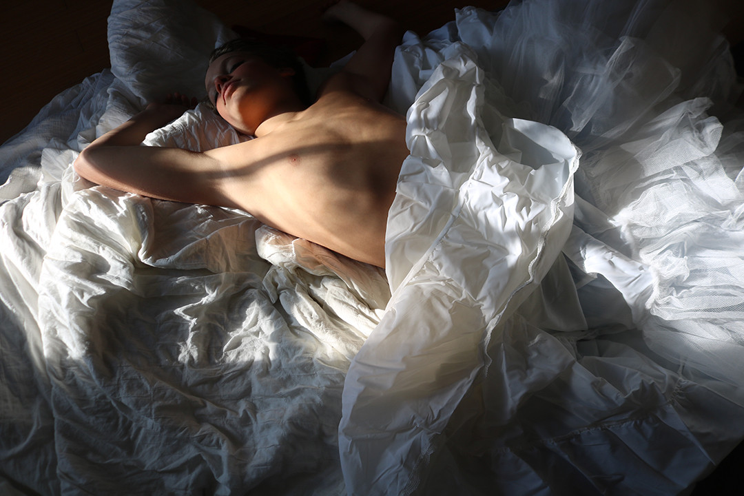 Photo of the light going across someone's body as they lay in a bed of white sheets