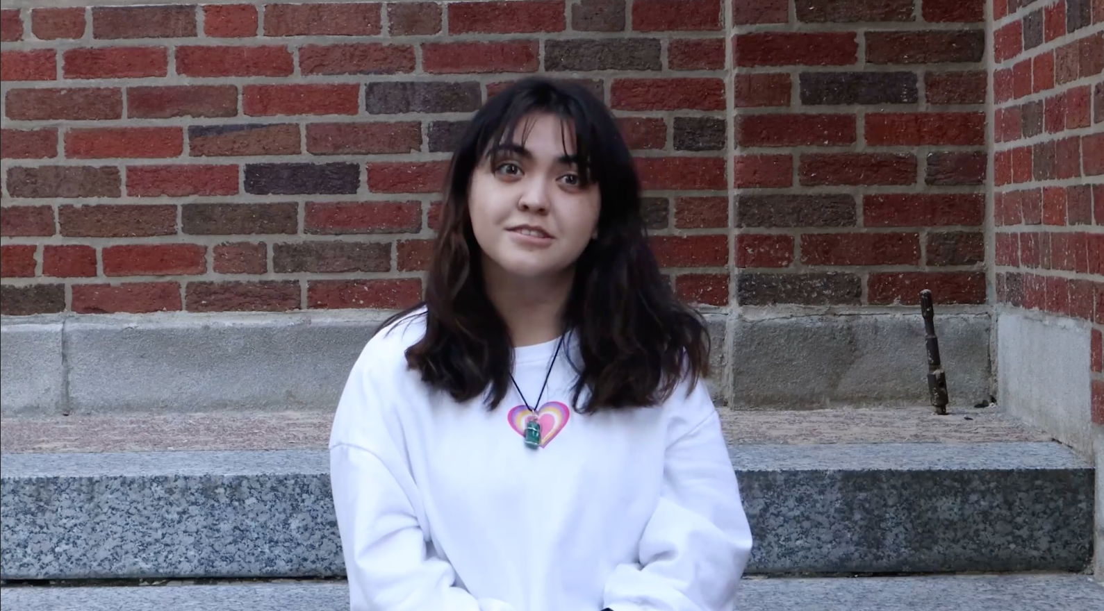 Picture of a person in a white sweater in front of a brick wall