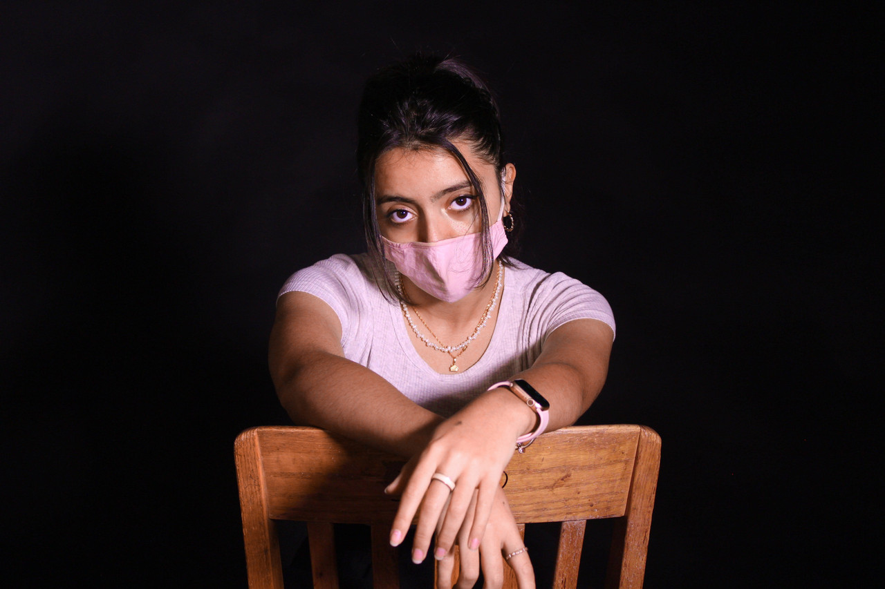 photo of a young woman seated backwards in school chair wearing a face covering