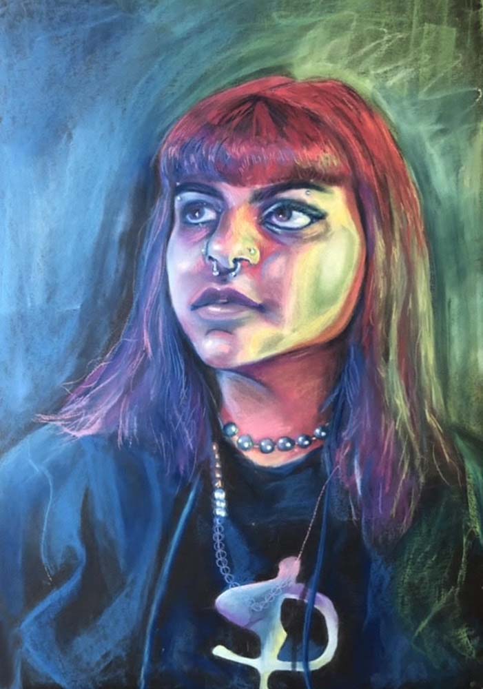 Person with long hair and bangs, wearing large necklaces and a septum piercing